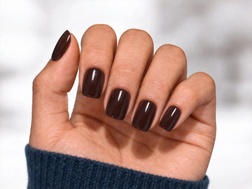 A relaxed palm-facing view of a hand wearing dark espresso brown press-on nails with a high-gloss finish and a modern short square shape.