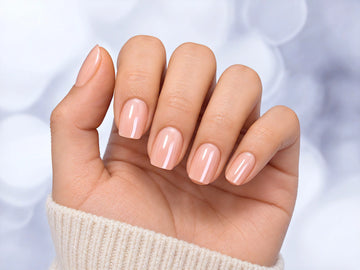 Hand held in a relaxed pose showing short square pearlescent pink chrome press-on nails with a glowing iridescent effect.