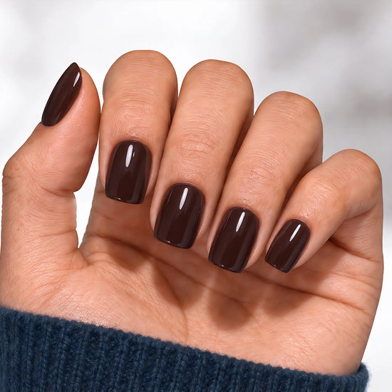 A relaxed palm-facing view of a hand wearing dark espresso brown press-on nails with a high-gloss finish and a modern short square shape.