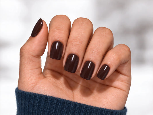 A relaxed palm-facing view of a hand wearing dark espresso brown press-on nails with a high-gloss finish and a modern short square shape.