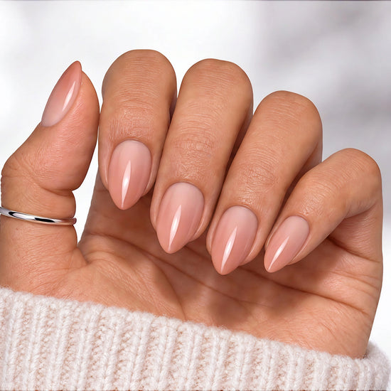 Hand held with palm facing viewer showing nude-to-pink gradient ombre press-on nails in a sophisticated short almond shape.