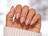 Hand held with palm facing viewer showing nude-to-pink gradient ombre press-on nails in a sophisticated short almond shape.