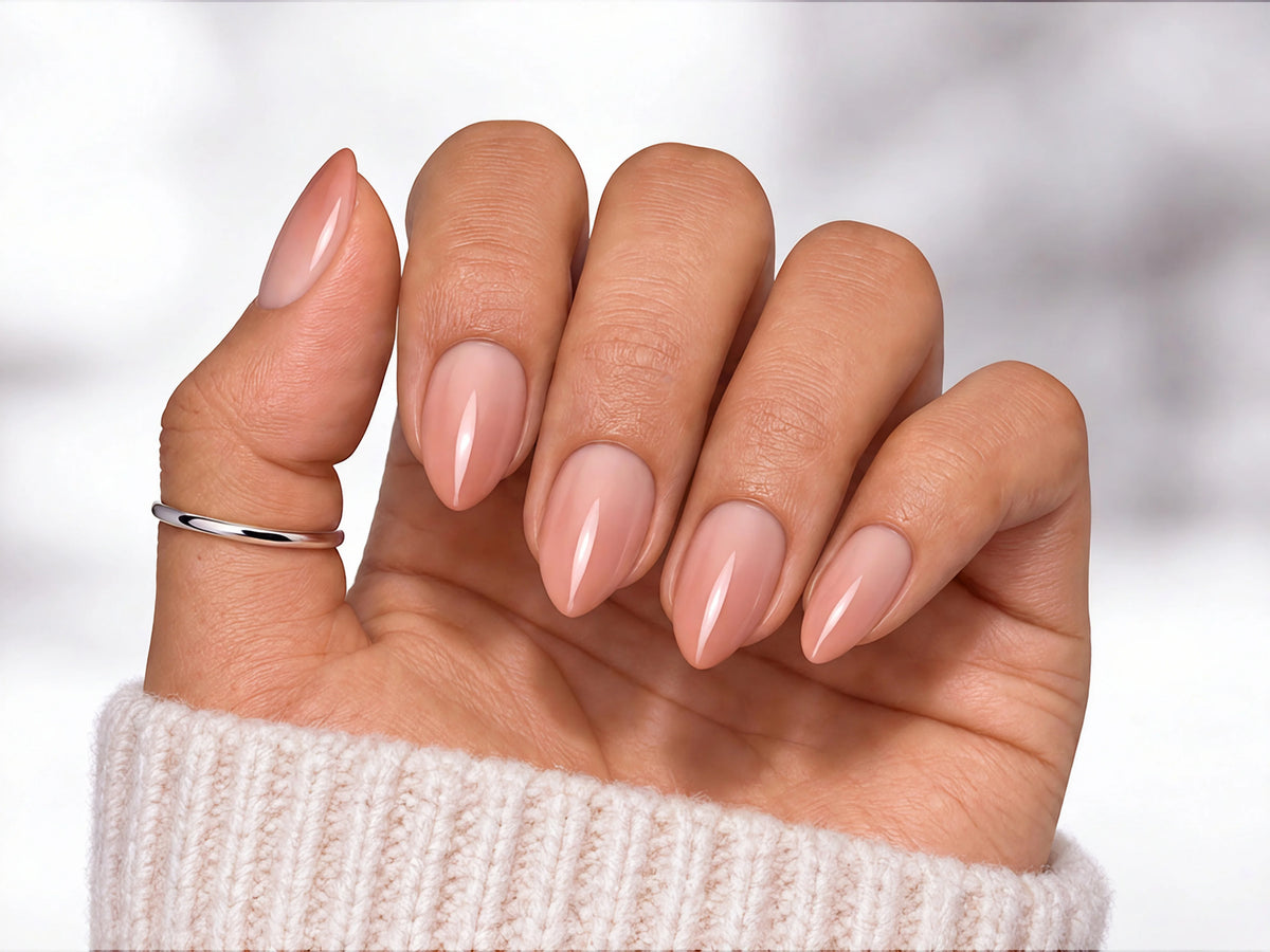 Hand held with palm facing viewer showing nude-to-pink gradient ombre press-on nails in a sophisticated short almond shape.