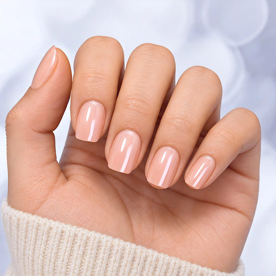 Hand held in a relaxed pose showing short square pearlescent pink chrome press-on nails with a glowing iridescent effect.