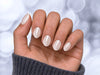 A palm-forward shot showing pearlescent white chrome extra short almond press-on nails with a clean, ethereal iridescent glow.